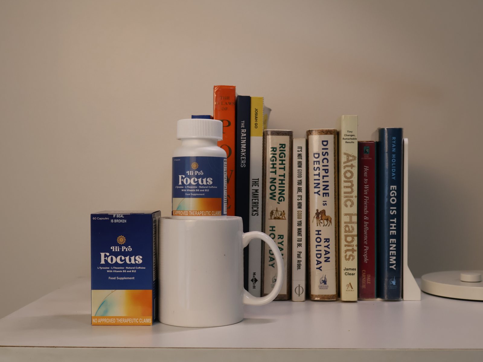 A bottle and box of Hi-Pro Focus on a coffee mug beside a row of books