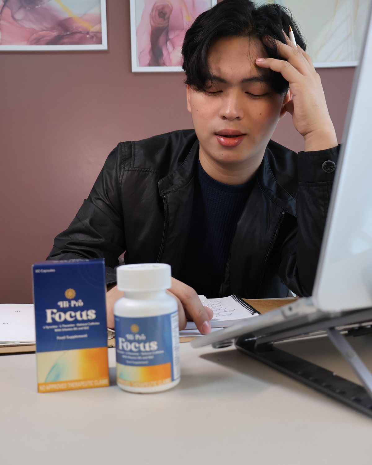 A man at his desk with his hand in his hair, too tired to focus, a bottle and box of Hi-Pro Focus beside him