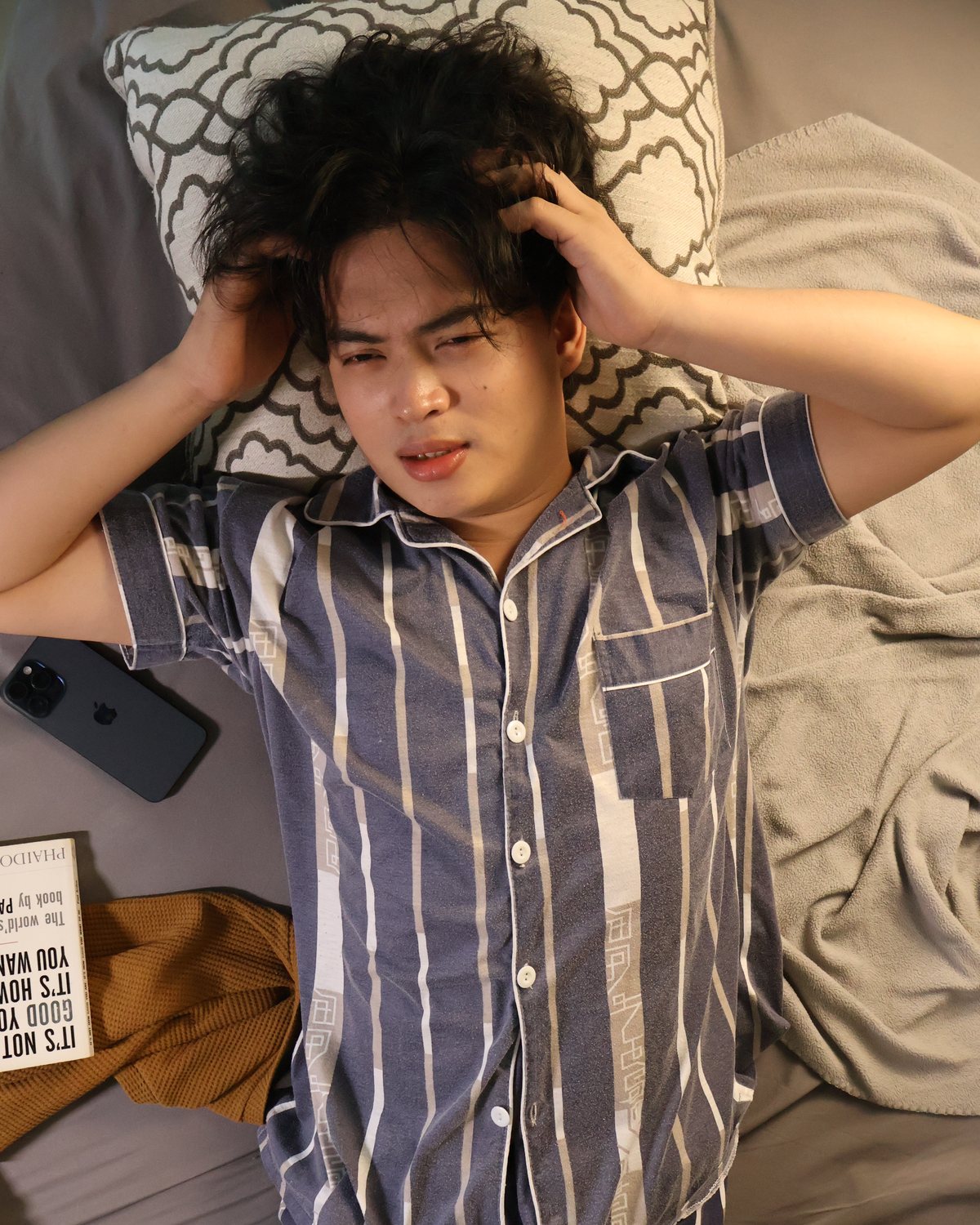 A man lying awake in bed with both hands in his hair, unable to switch off